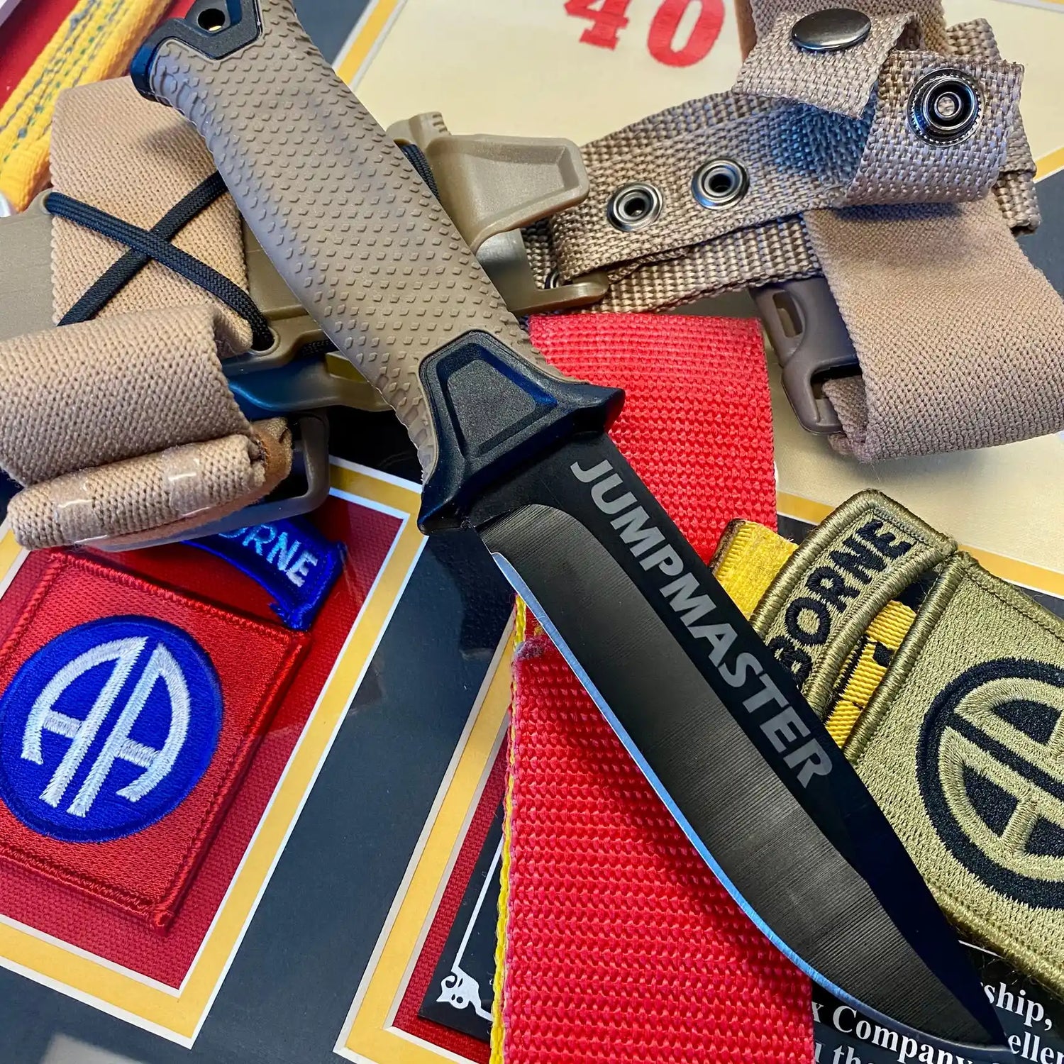Jumpmaster Knife, Jumpmaster Knives. Knife built for Jumpmaster Duties. Knife with 'Jumpmaster' branding on a background of colorful patches and straps